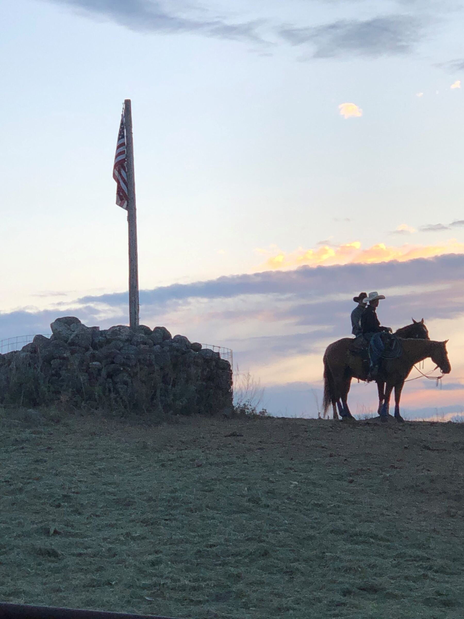 Two riders on horseback beside an American flag at sunset